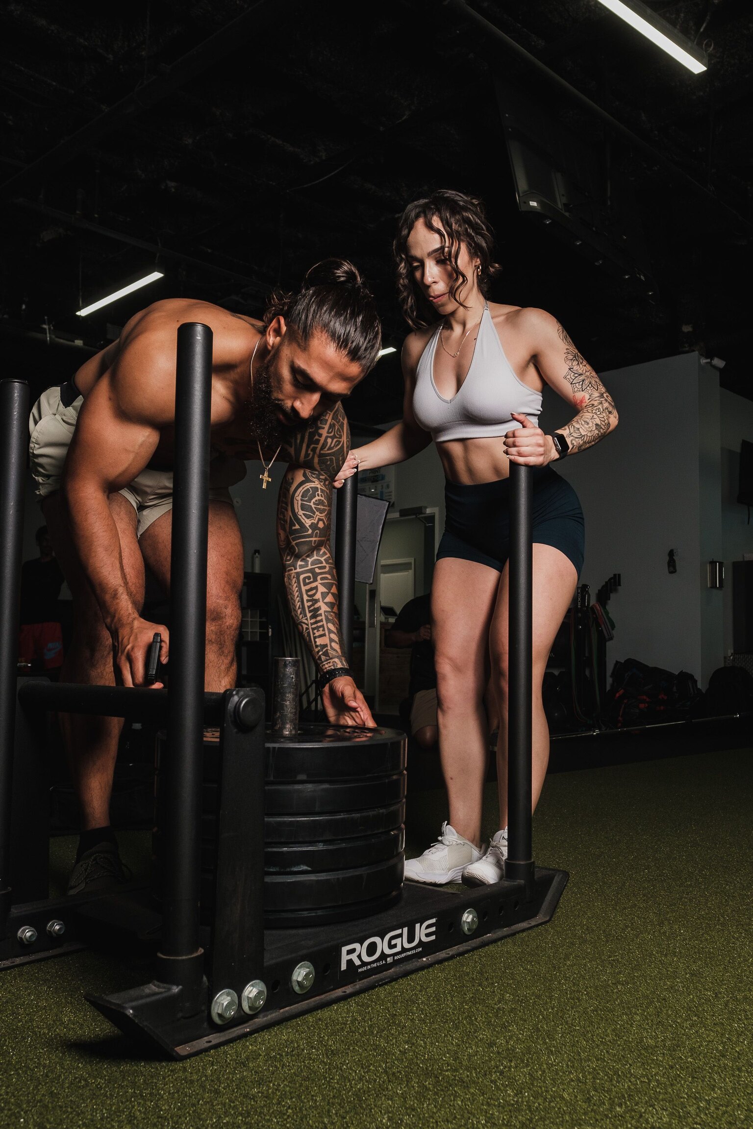 A trainer and client adjusting a weighted sled in a gym