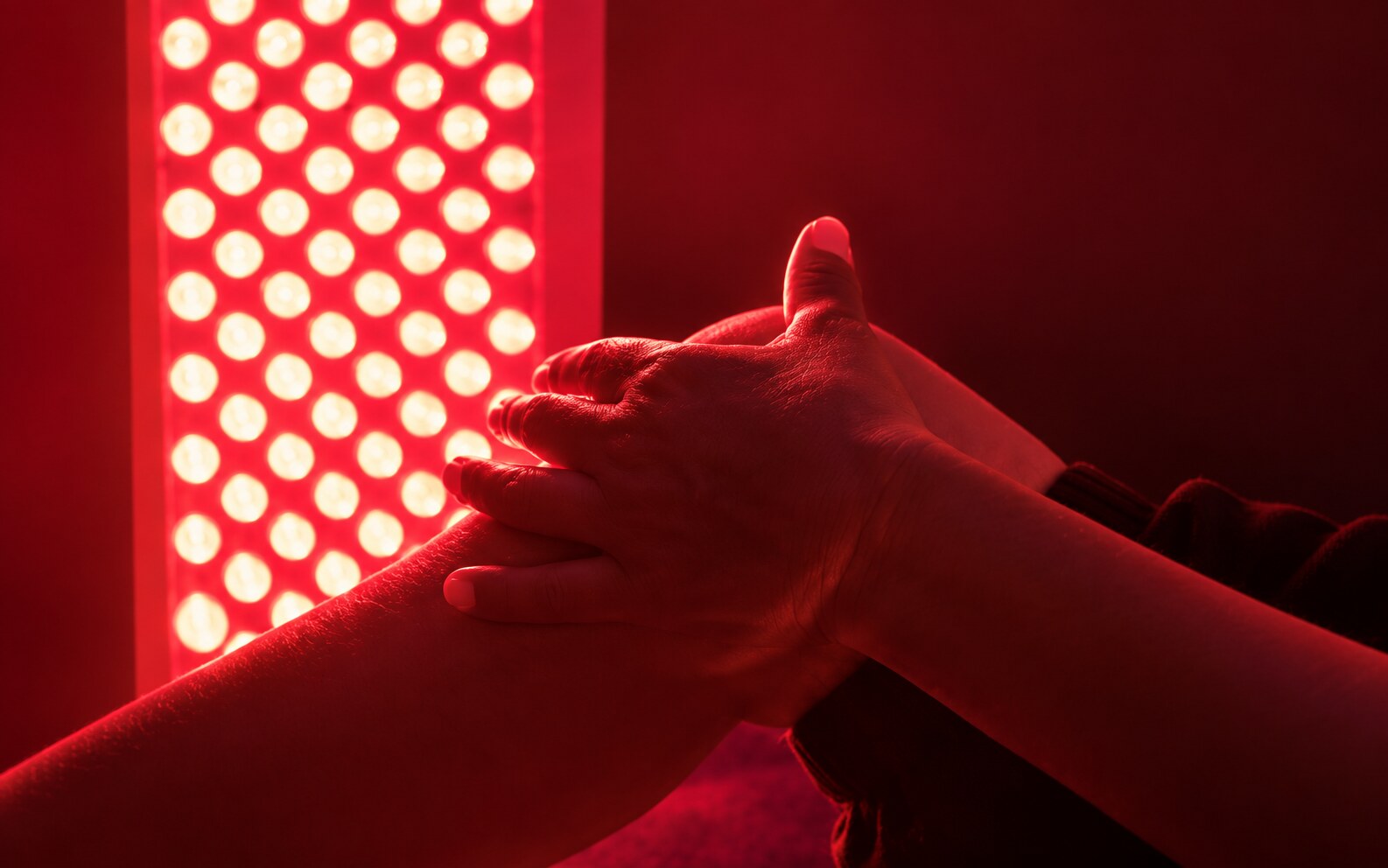 Hands resting beside a red-light therapy panel